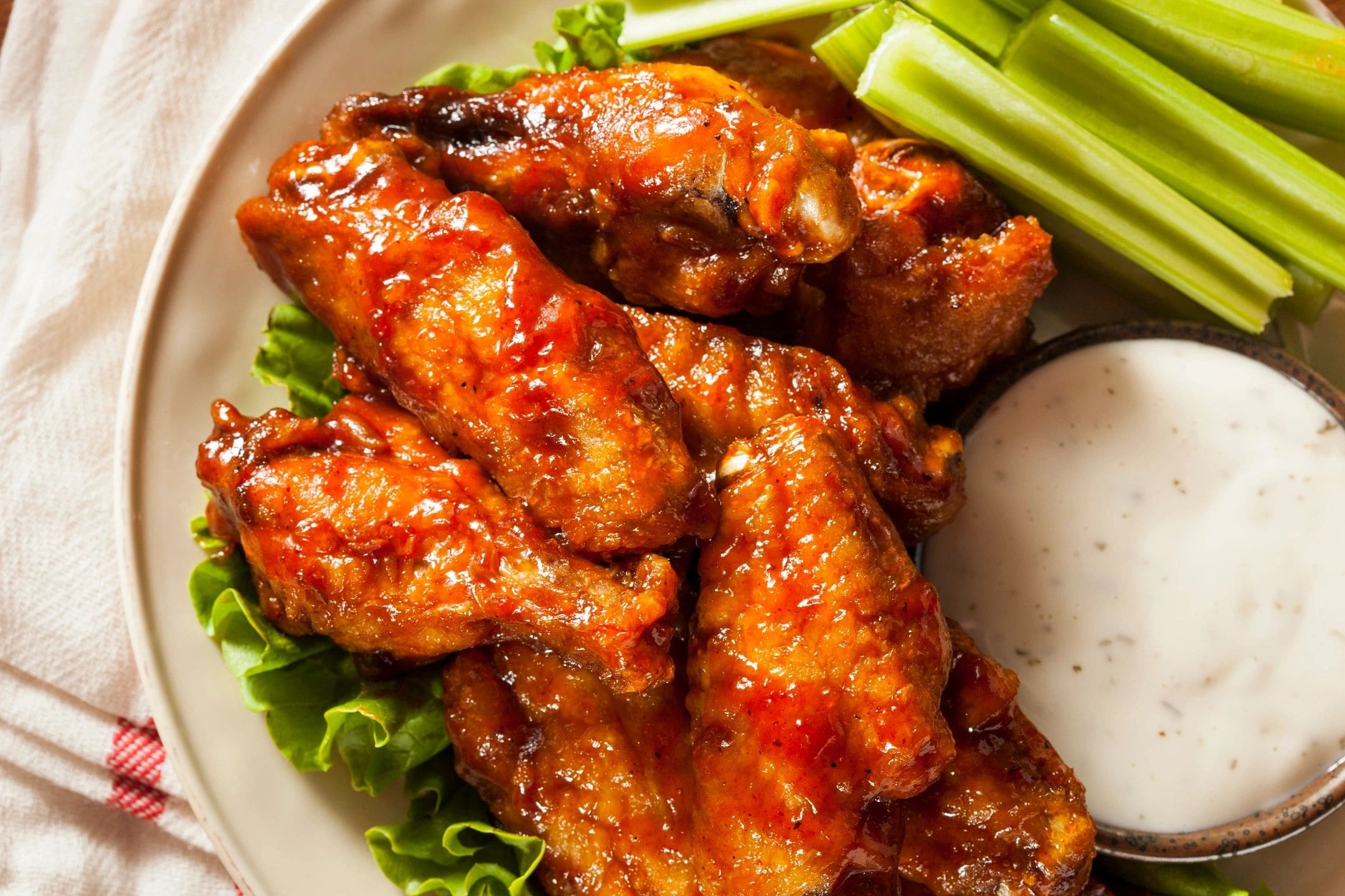 A plate of chicken wings with celery and sauce.